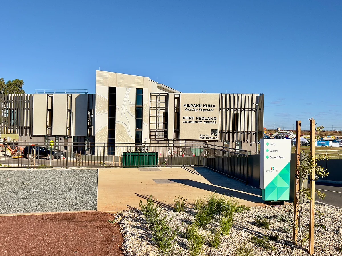 The Milpaku Kuma Port Hedland Community Centre, a modern building with vertical timber fins and the words Coming Together on its facade, under a clear blue sky