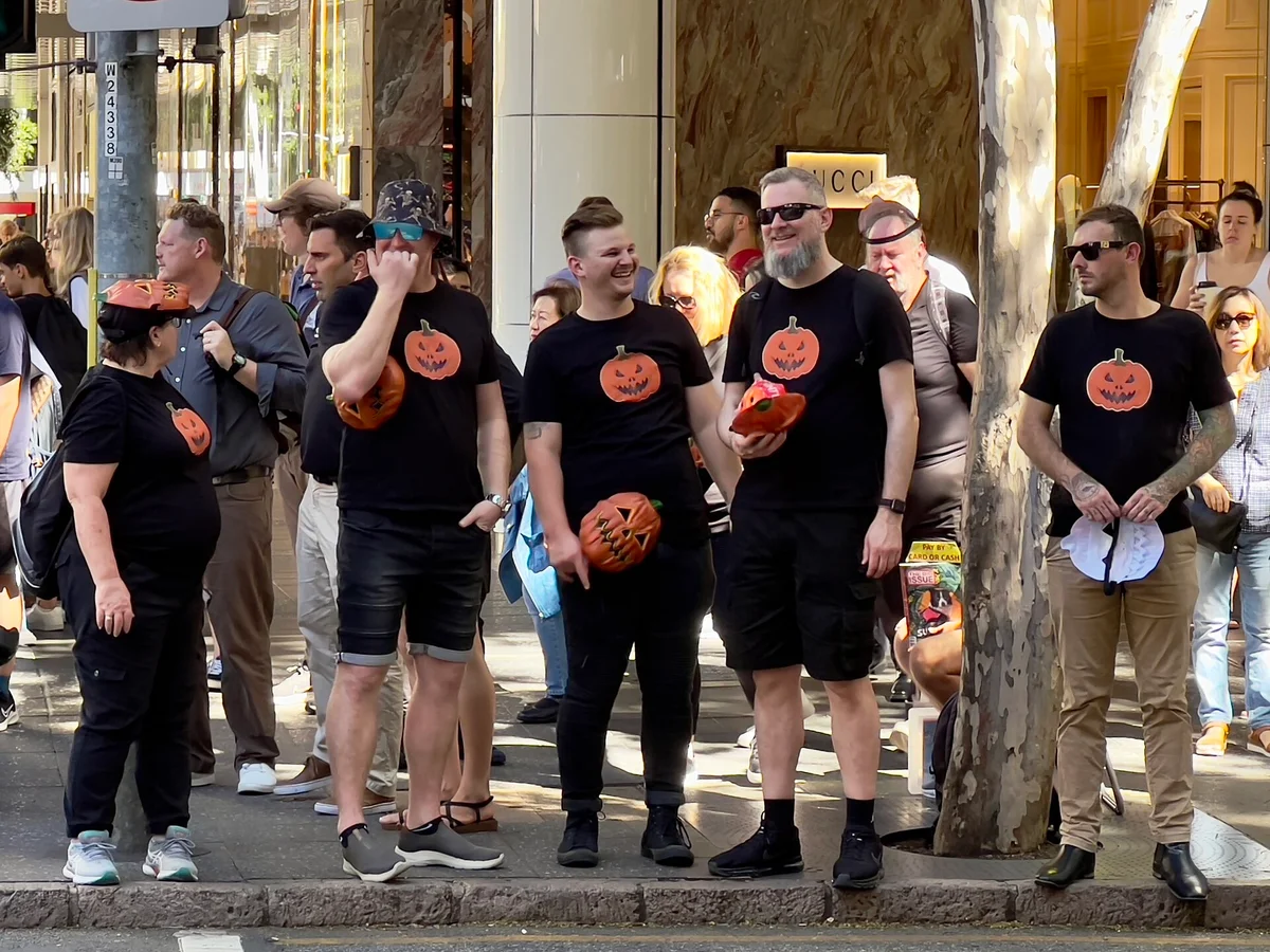 A group of people in matching pumpkin T-shirts on a city footpath