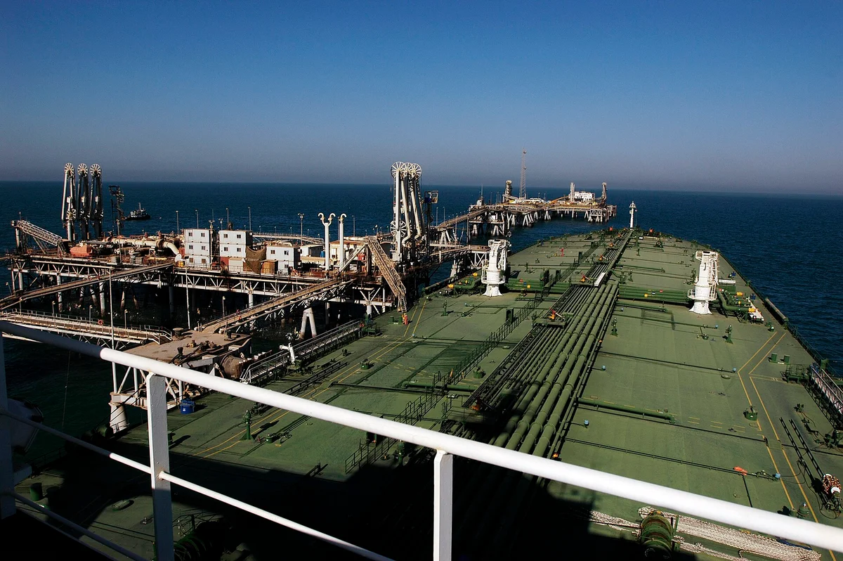 A large oil tanker moored alongside an offshore oil loading terminal in the Persian Gulf, seen from the water with loading arms connected