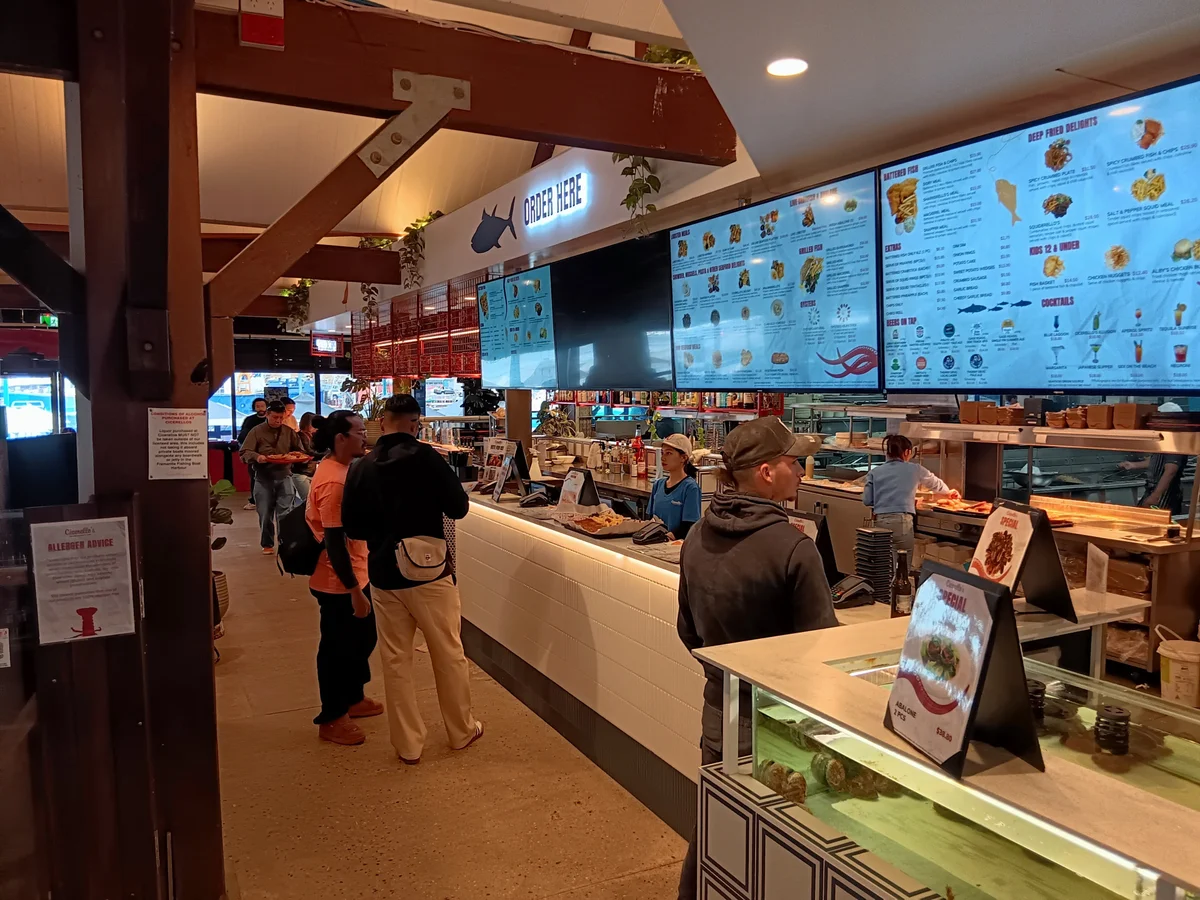 Customers ordering at the counter at Cicerello's beneath digital menu boards