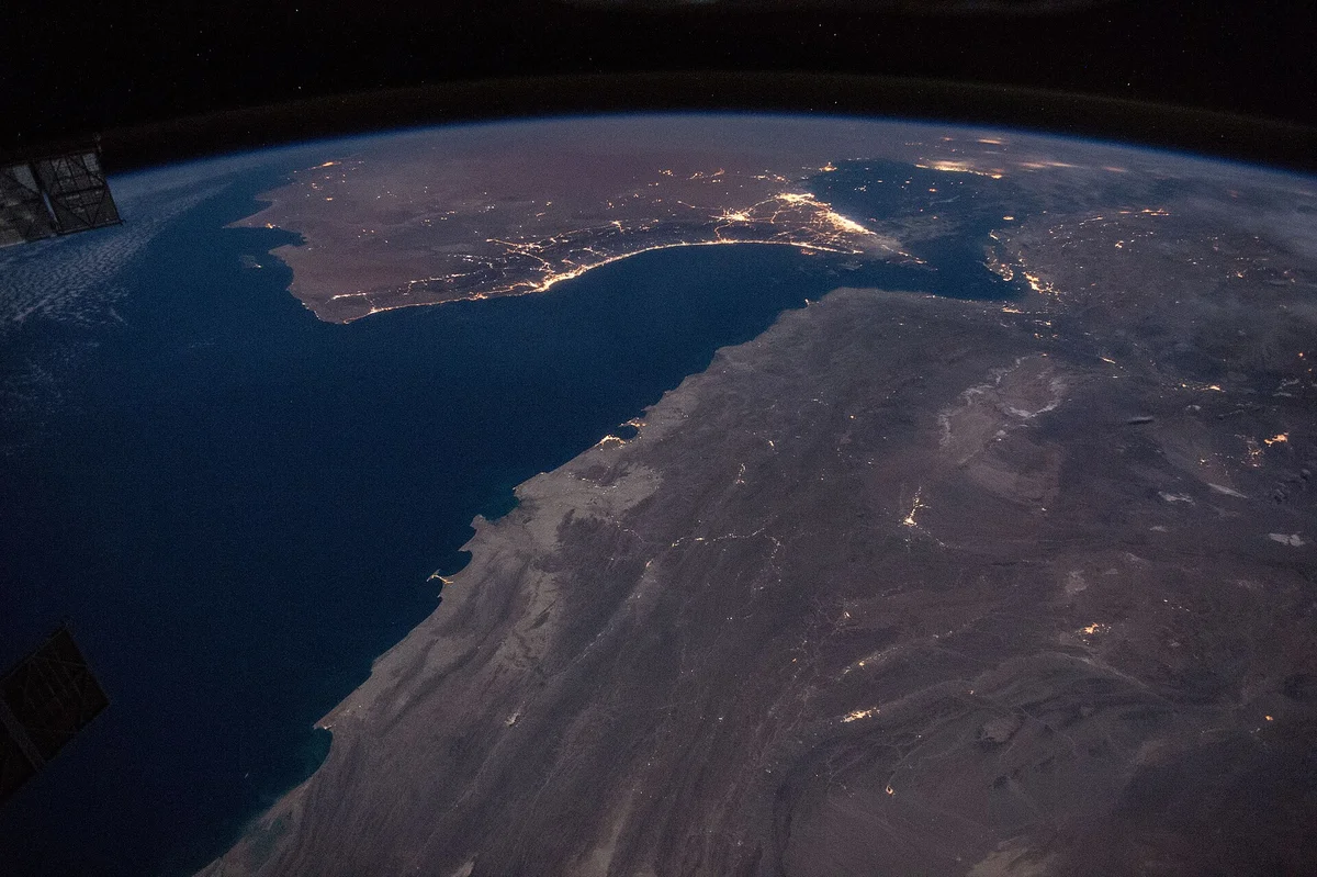 Night photograph from the International Space Station looking across the Gulf of Oman, with the coastal city lights of Muscat, Dubai, Abu Dhabi and Doha and the dark water of the Strait of Hormuz