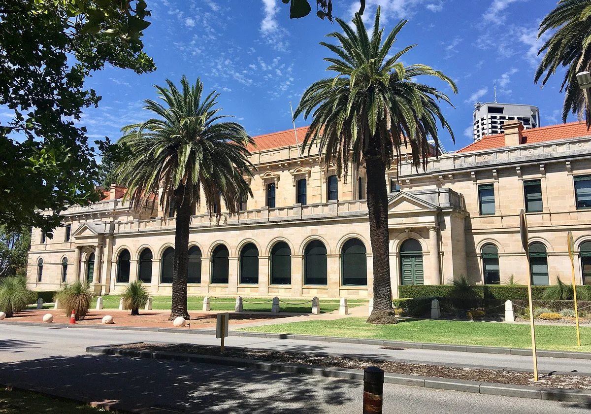 The west side of Parliament House in West Perth, a stone building with columns and a flagpole, under a blue sky