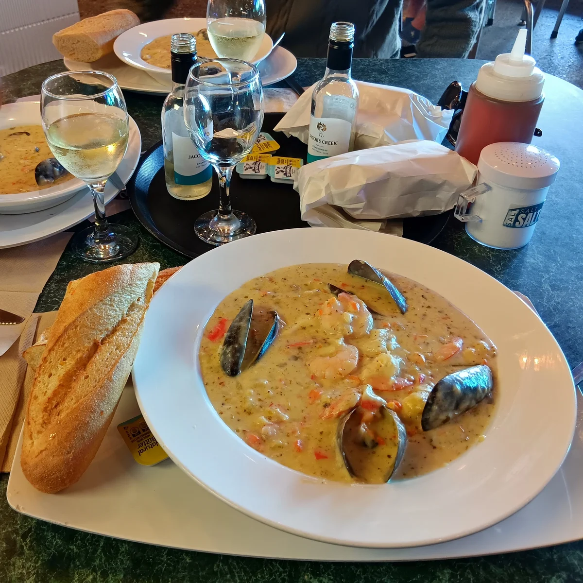 A large bowl of seafood chowder with mussels and a crusty bread roll at Cicerello's
