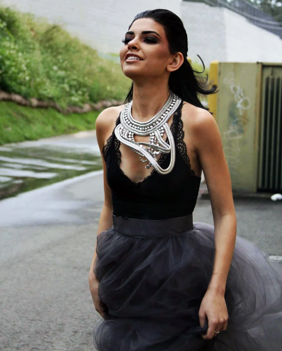 A woman in a black top and dark tulle skirt wearing a large silver statement necklace