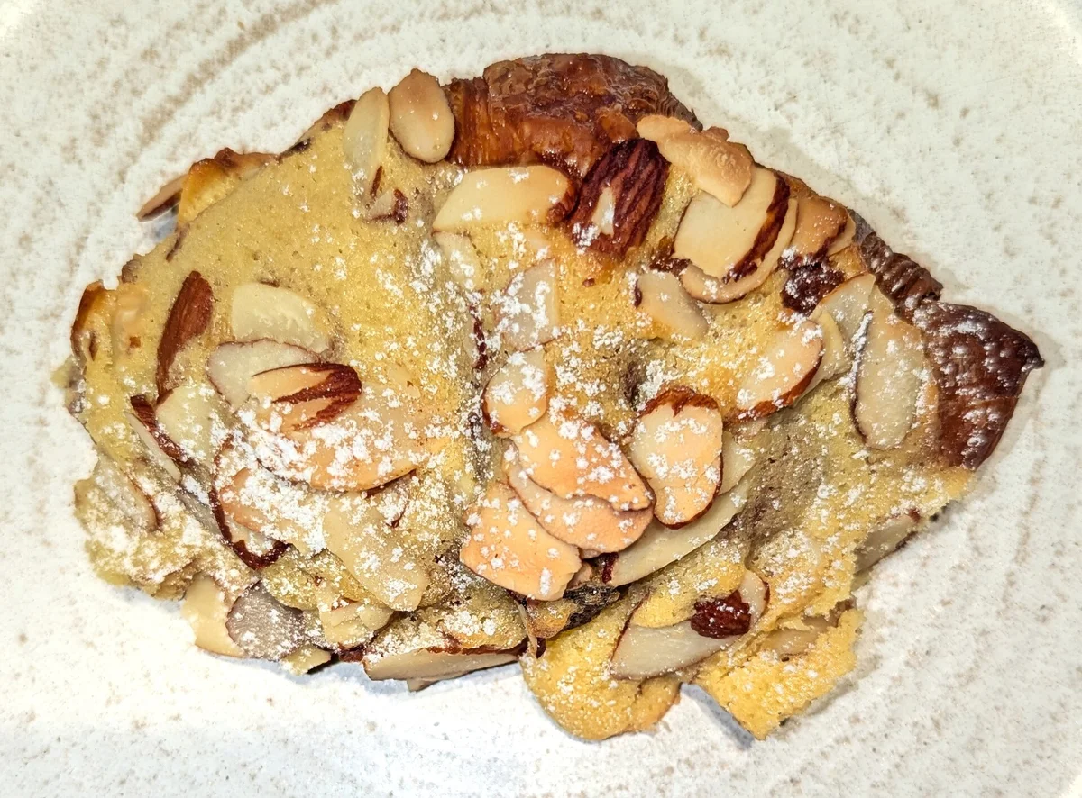 An almond croissant topped with flaked almonds and icing sugar
