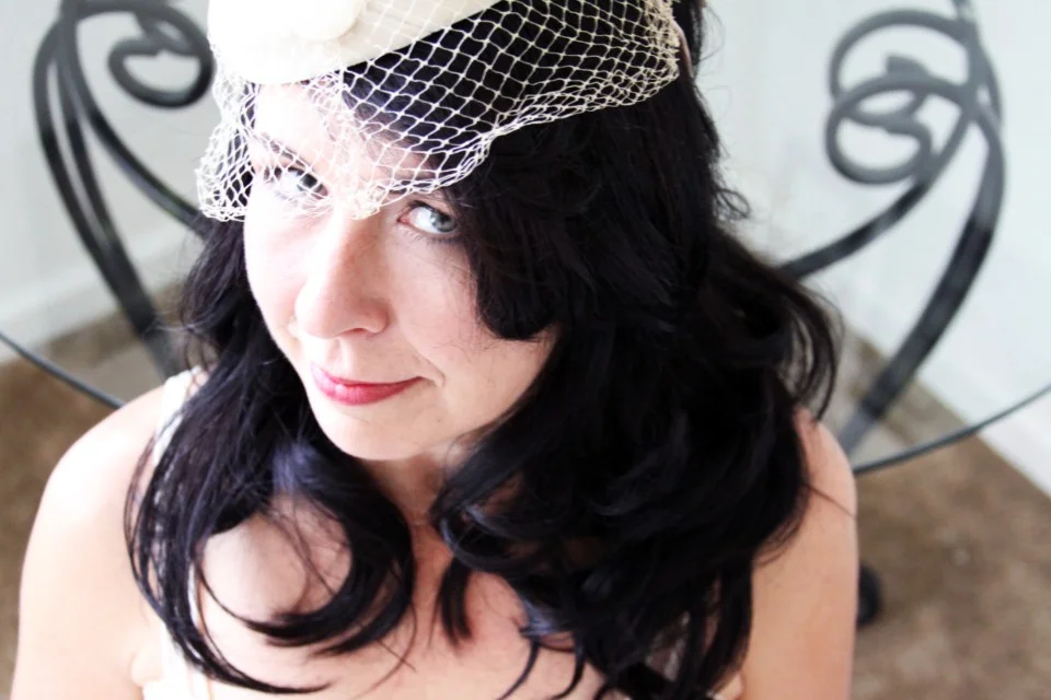 A woman with dark hair wearing a cream fascinator with a netted veil